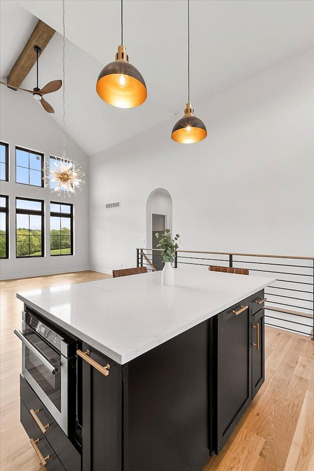 kitchen with dark cabinets, light wood-style flooring, a ceiling fan, high vaulted ceiling, and visible vents
