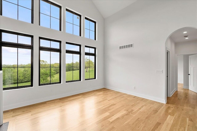 unfurnished living room with high vaulted ceiling, visible vents, light wood-style flooring, arched walkways, and baseboards