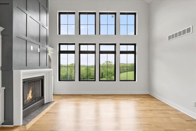 unfurnished living room featuring a healthy amount of sunlight, a towering ceiling, a fireplace with flush hearth, and visible vents