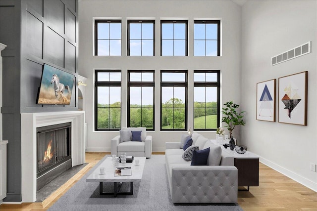 living room with light wood-type flooring, a fireplace with flush hearth, visible vents, and a high ceiling