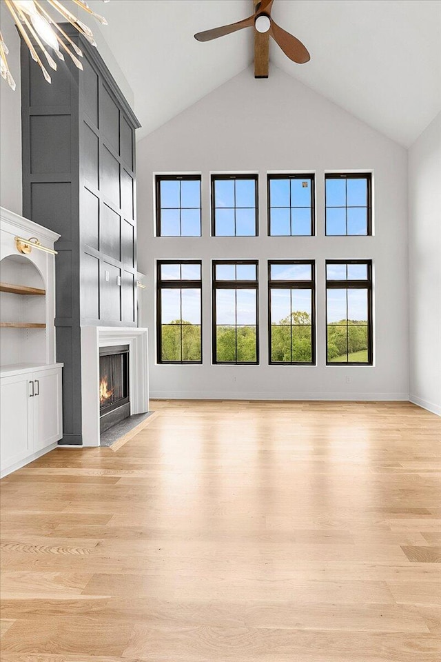 unfurnished living room featuring light wood-type flooring, ceiling fan, a fireplace with flush hearth, and high vaulted ceiling