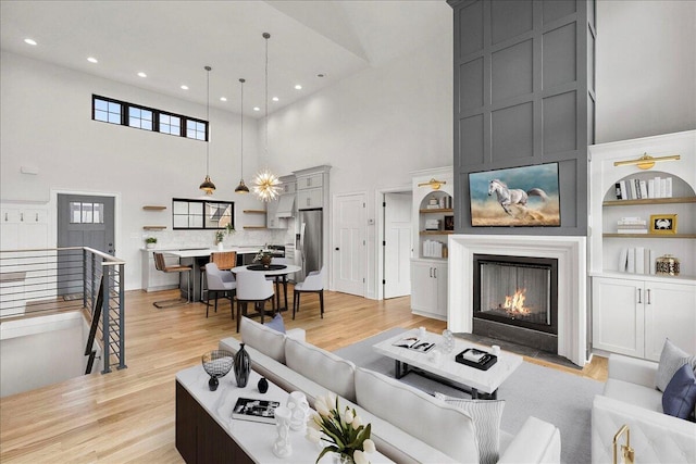 living room featuring light wood-style floors, a fireplace, recessed lighting, and a high ceiling