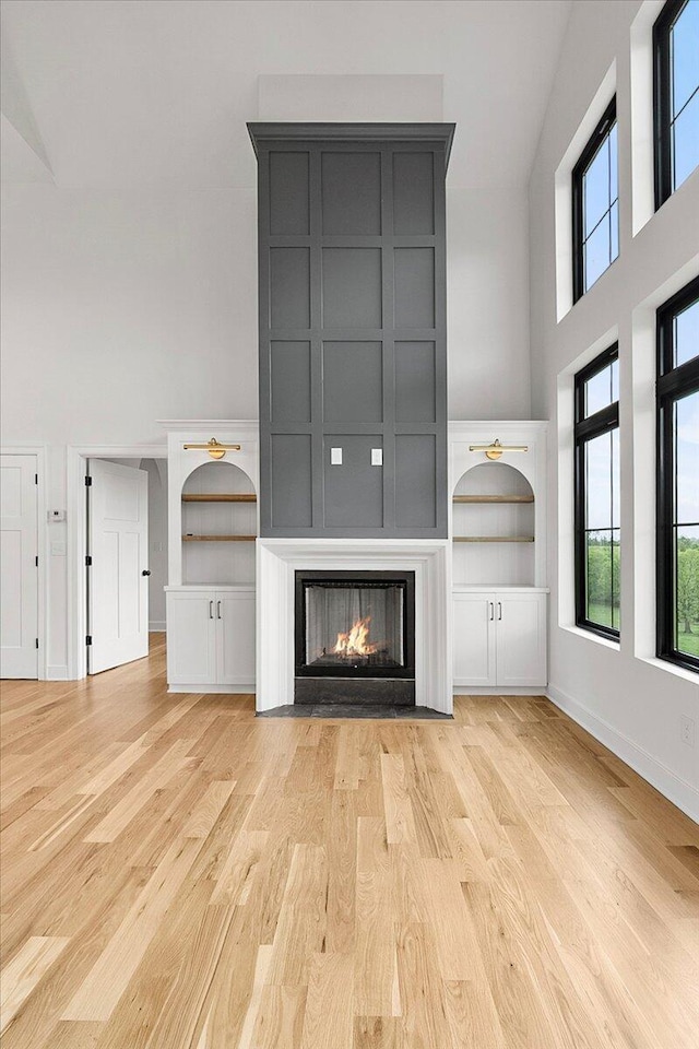 unfurnished living room with a lit fireplace, wood finished floors, baseboards, and a high ceiling