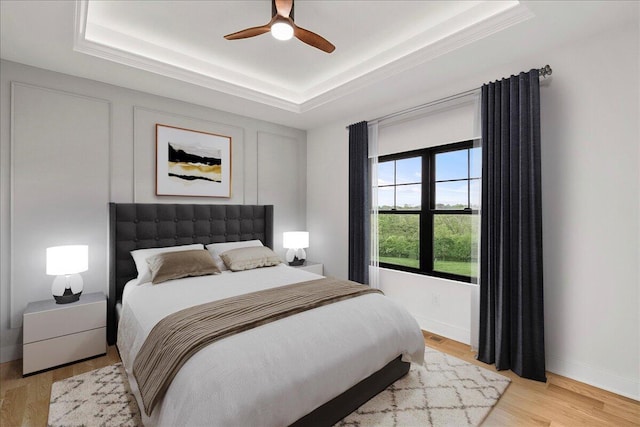 bedroom featuring ceiling fan, a raised ceiling, baseboards, and light wood-type flooring