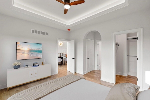 bedroom featuring a tray ceiling, arched walkways, visible vents, and wood finished floors