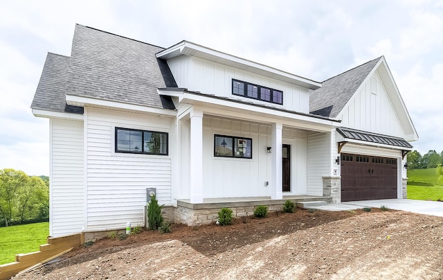 view of front of home featuring covered porch, roof with shingles, concrete driveway, metal roof, and board and batten siding
