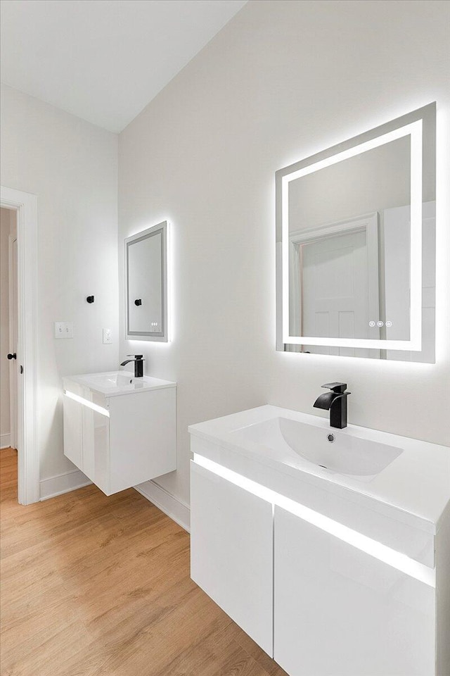 bathroom with a sink, two vanities, baseboards, and wood finished floors