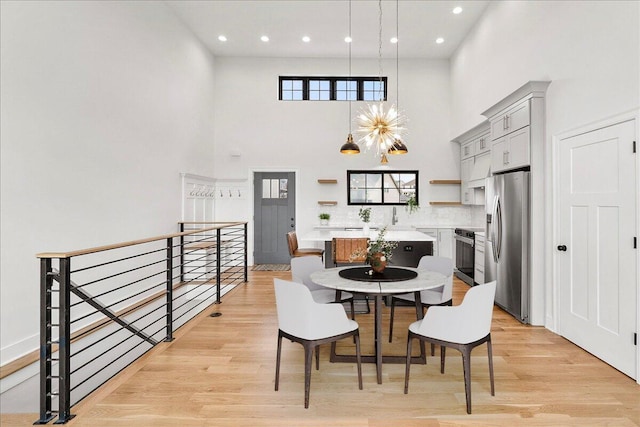 dining area featuring light wood finished floors, recessed lighting, and a high ceiling