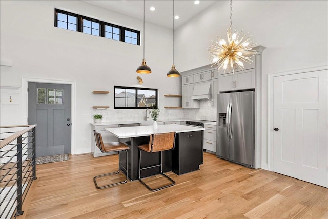 kitchen with custom exhaust hood, stainless steel fridge, open shelves, a towering ceiling, and light countertops