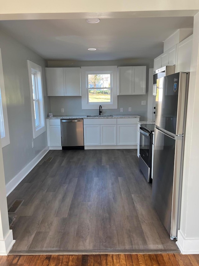 kitchen featuring appliances with stainless steel finishes, light stone counters, dark wood-type flooring, sink, and white cabinets