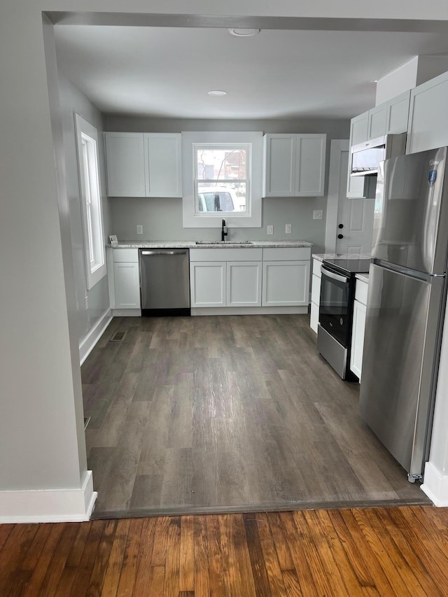 kitchen with appliances with stainless steel finishes, dark wood-type flooring, sink, white cabinets, and plenty of natural light