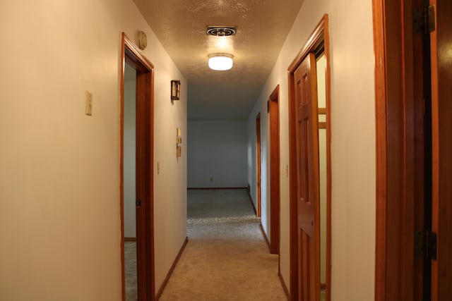 corridor with light colored carpet and a textured ceiling