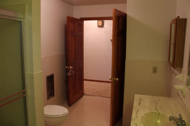 bathroom with sink, toilet, a shower with shower door, and tile walls