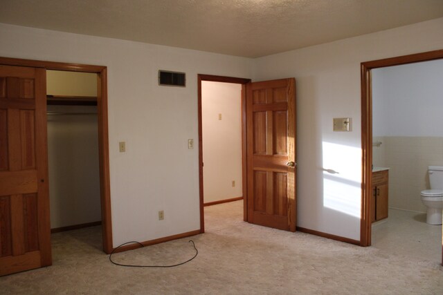 unfurnished bedroom featuring a walk in closet, a textured ceiling, light colored carpet, connected bathroom, and a closet