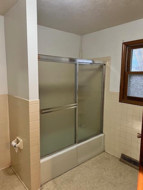 bathroom with a textured ceiling, enclosed tub / shower combo, and tile walls