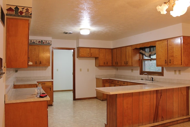 kitchen with backsplash, sink, a textured ceiling, a notable chandelier, and kitchen peninsula