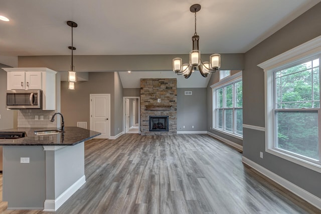 kitchen featuring a fireplace, dark stone counters, backsplash, decorative light fixtures, and white cabinets