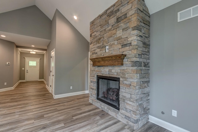 unfurnished living room featuring a stone fireplace, light wood-type flooring, and high vaulted ceiling