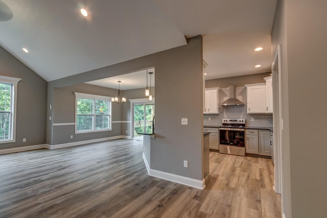 kitchen featuring stainless steel electric range, a healthy amount of sunlight, white cabinets, and wall chimney range hood