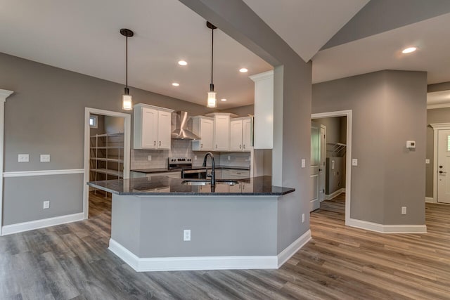 kitchen featuring dark wood-type flooring, white cabinetry, hanging light fixtures, dark stone countertops, and wall chimney exhaust hood