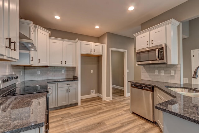 kitchen with wall chimney range hood, white cabinetry, sink, and appliances with stainless steel finishes