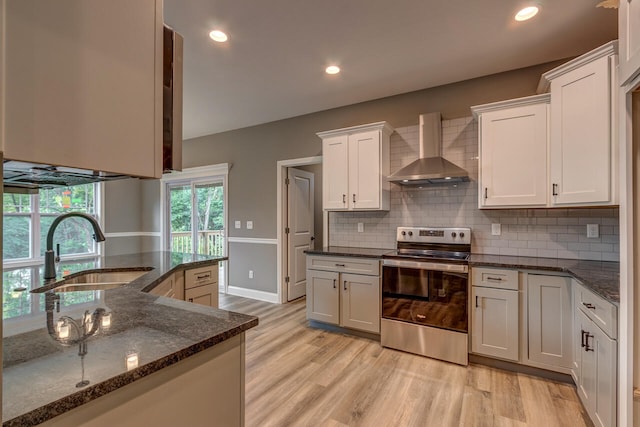 kitchen featuring white cabinetry, wall chimney range hood, stainless steel electric range oven, sink, and light hardwood / wood-style flooring