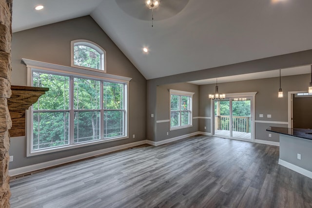 unfurnished living room with high vaulted ceiling, ceiling fan with notable chandelier, and wood-type flooring