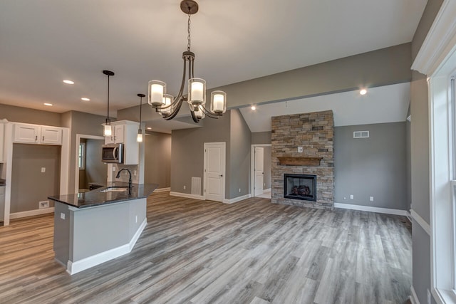 kitchen featuring sink, a stone fireplace, white cabinets, pendant lighting, and vaulted ceiling