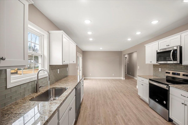 kitchen with backsplash, white cabinets, sink, appliances with stainless steel finishes, and light hardwood / wood-style floors