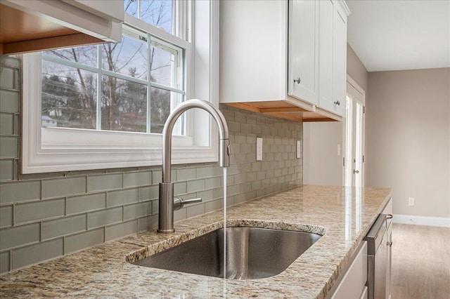 kitchen with sink, hardwood / wood-style flooring, light stone countertops, tasteful backsplash, and white cabinetry