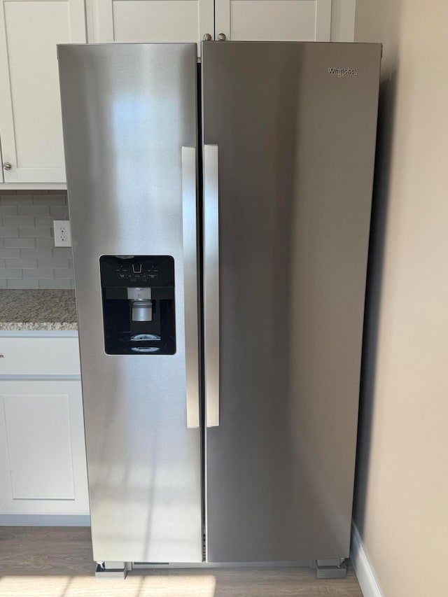 details with decorative backsplash, light wood-type flooring, light stone counters, white cabinets, and stainless steel fridge with ice dispenser