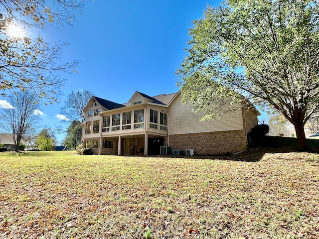 rear view of property with a sunroom, a yard, and central air condition unit