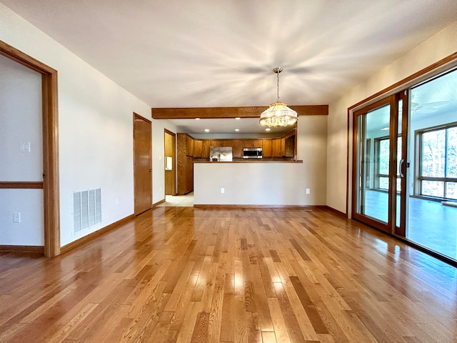 unfurnished living room with light wood-type flooring and an inviting chandelier