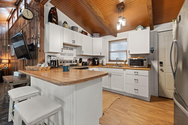 kitchen with a kitchen breakfast bar, vaulted ceiling with beams, wooden counters, white cabinets, and appliances with stainless steel finishes