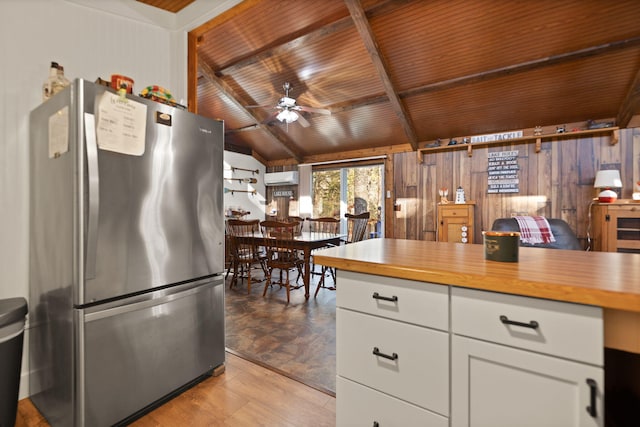 kitchen featuring ceiling fan, wooden ceiling, stainless steel fridge, wood walls, and white cabinets