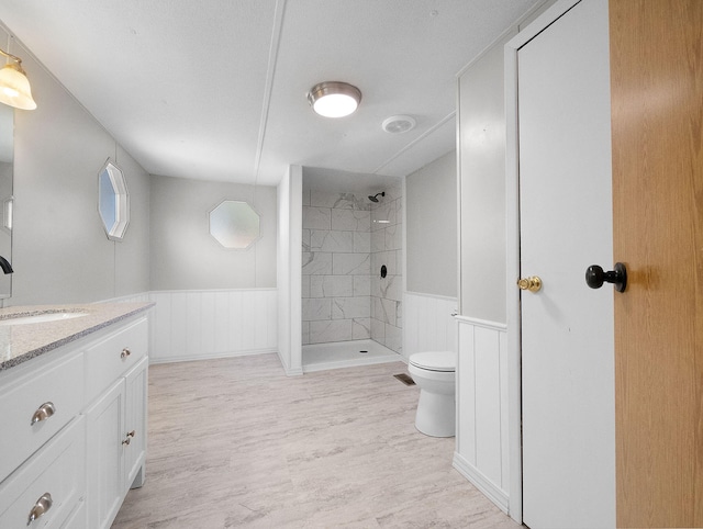 bathroom featuring a tile shower, vanity, toilet, and wood-type flooring