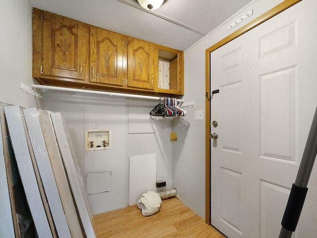 clothes washing area featuring cabinets, hookup for a washing machine, light hardwood / wood-style flooring, and a textured ceiling