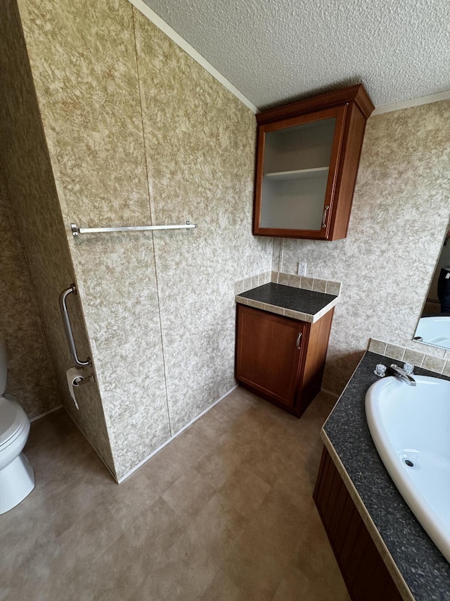 bathroom featuring vanity, toilet, ornamental molding, and a textured ceiling