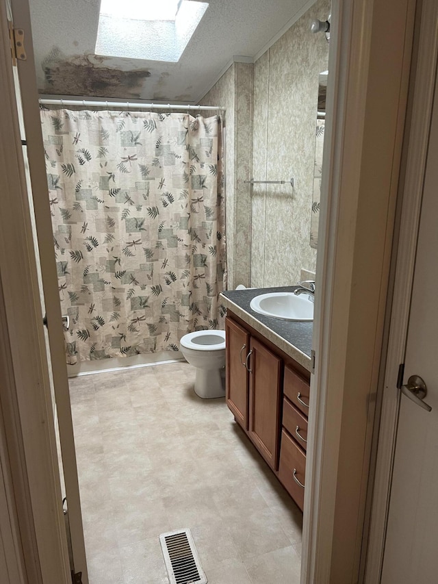 full bathroom with vanity, a skylight, toilet, ornamental molding, and a textured ceiling