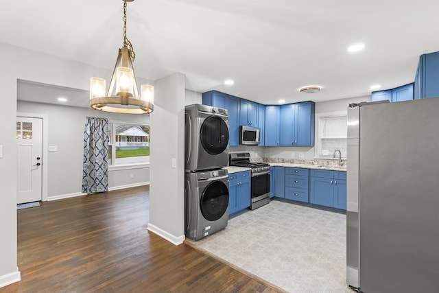 kitchen with appliances with stainless steel finishes, sink, pendant lighting, stacked washer / dryer, and light hardwood / wood-style floors