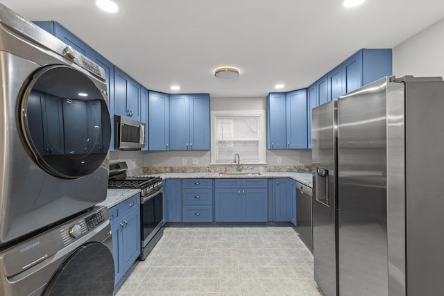 kitchen featuring blue cabinets, sink, appliances with stainless steel finishes, light stone counters, and stacked washer / dryer