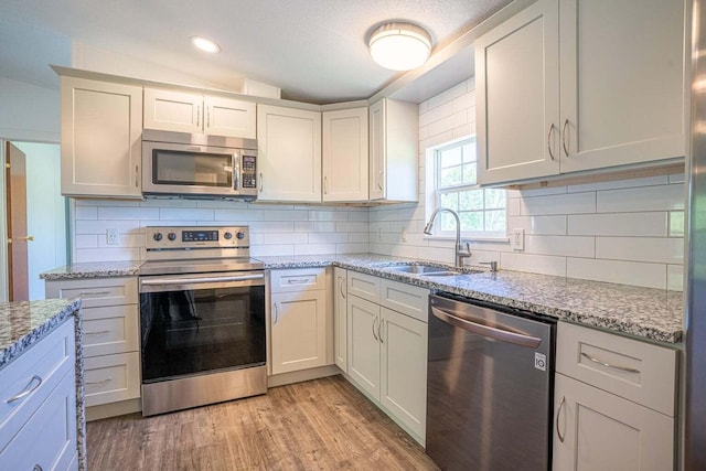 kitchen featuring stainless steel appliances, light stone counters, sink, white cabinetry, and light wood-type flooring