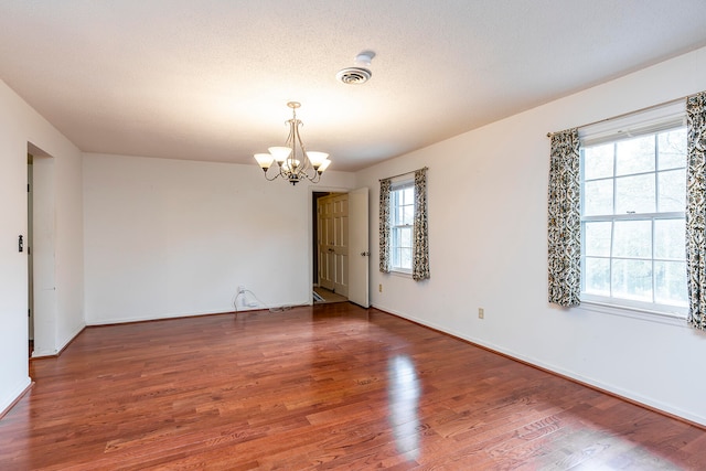 unfurnished room featuring an inviting chandelier, wood-type flooring, and a textured ceiling