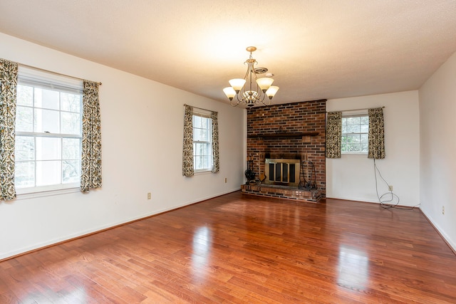 unfurnished living room with a fireplace, wood-type flooring, a textured ceiling, and an inviting chandelier