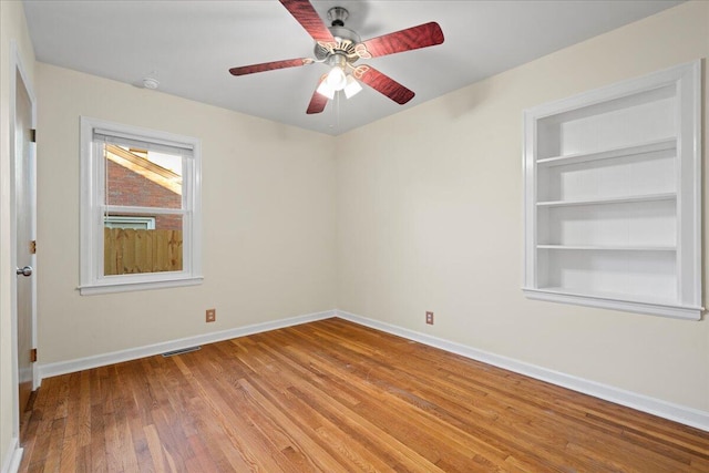 unfurnished room featuring light hardwood / wood-style flooring, ceiling fan, and built in shelves