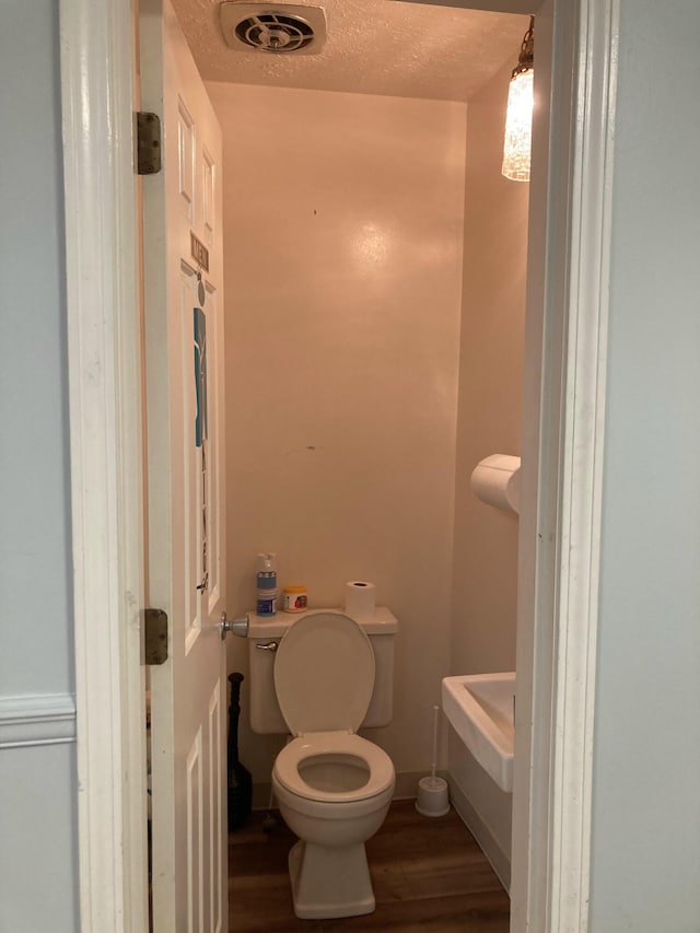 bathroom with hardwood / wood-style floors, a textured ceiling, and toilet