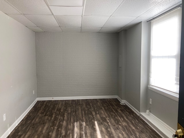 unfurnished room with a paneled ceiling, dark wood-type flooring, and brick wall