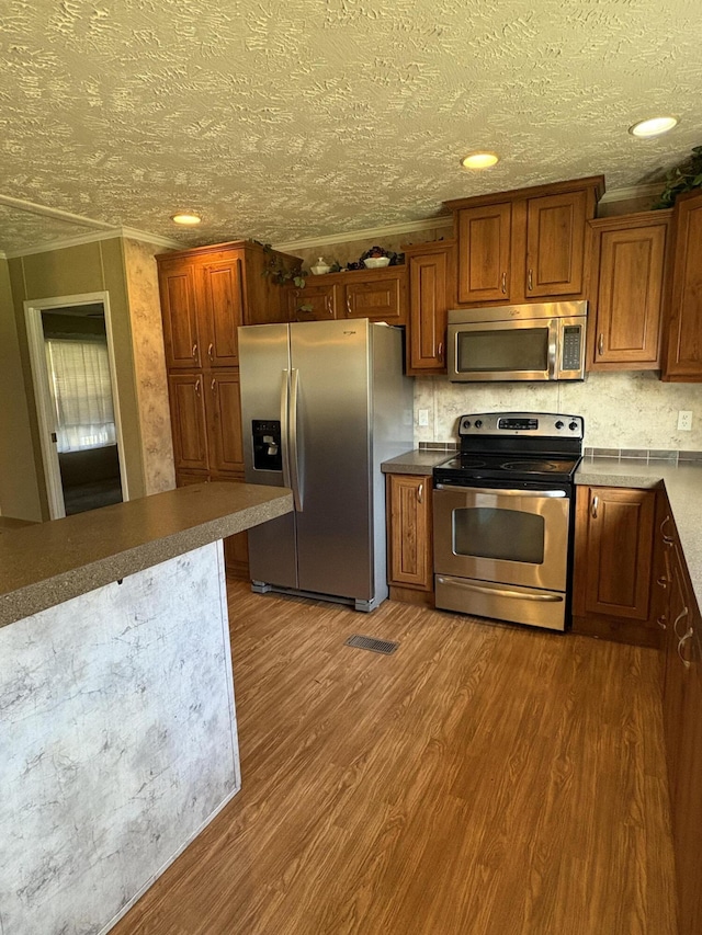 580 Bales Creek Rd, Manchester, KY 40962 - kitchen with stainless steel appliances, wood finished floors, brown cabinets, a textured ceiling, and crown molding