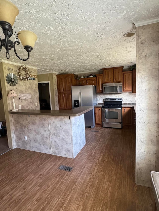 kitchen featuring kitchen peninsula, appliances with stainless steel finishes, a kitchen breakfast bar, dark hardwood / wood-style floors, and a textured ceiling