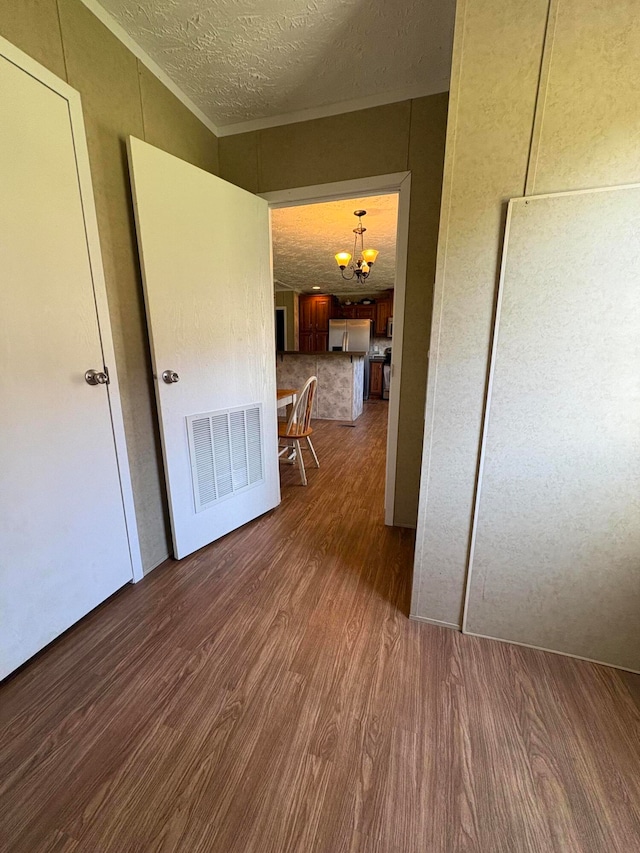 corridor with dark hardwood / wood-style floors, a textured ceiling, crown molding, and a notable chandelier